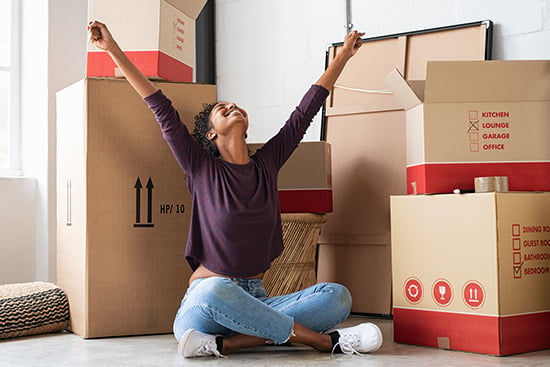 Excited young woman sitting with moving boxes in new home