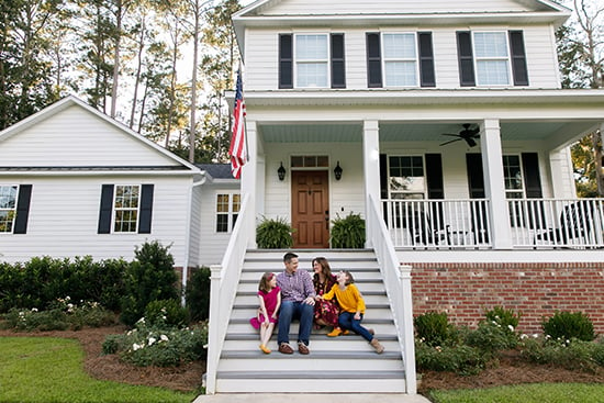 Family sitting on front steps of new house