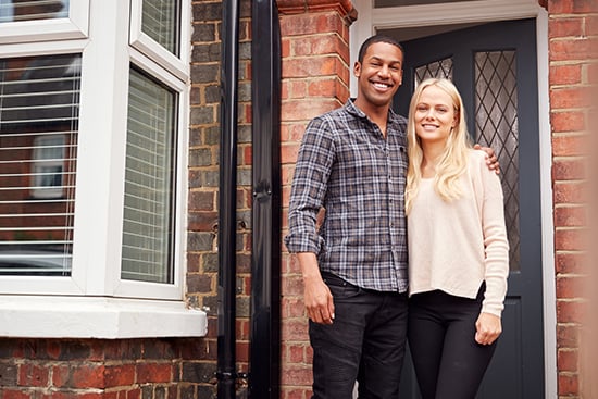 Proud young couple standing in front of their home